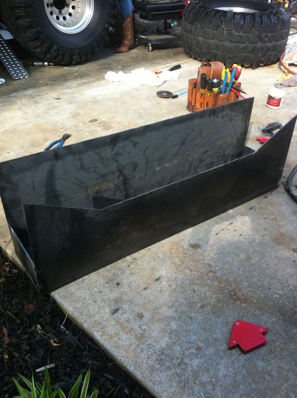 Metal fabrication parts on concrete, with large tires and tools in background