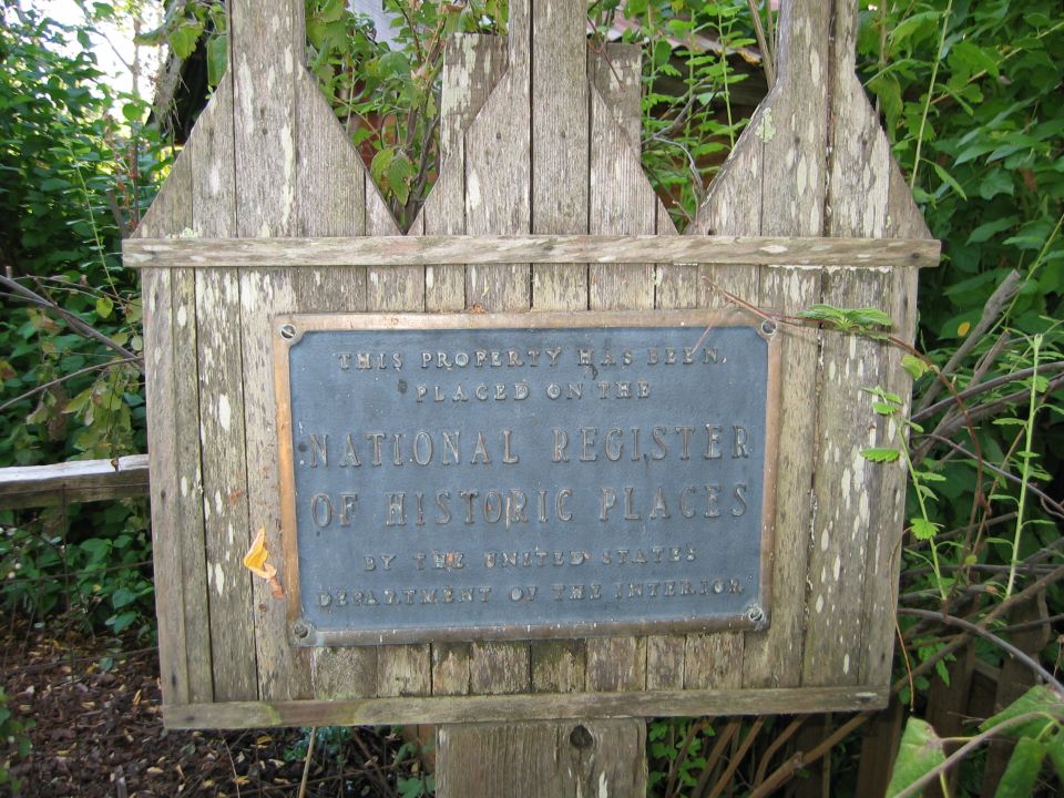 National Register of Historic Places metal plaque on weathered wooden signboard