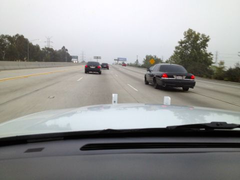 2004 Ford Crown Victoria - A black sedan is seen driving on a highway with other vehicles in the distance on a foggy day.
