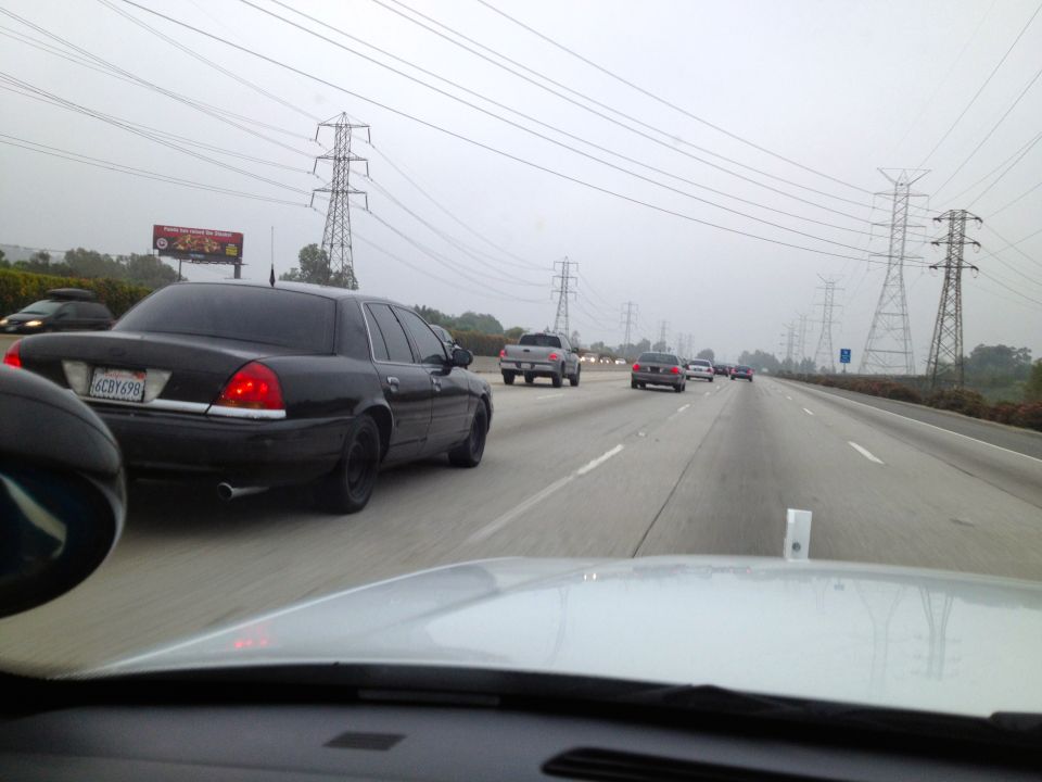 Black Ford Crown Victoria driving on highway, license plate 6CDY699. Other cars and power lines visible