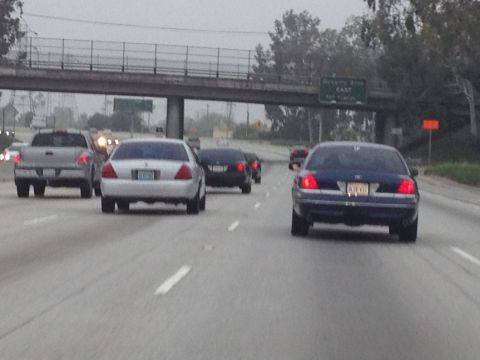 2004 Ford Crown Victoria - A silver 2004 Ford Crown Victoria is seen from behind on a highway, with other vehicles also present.