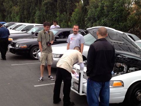 2004 Ford Crown Victoria - Several people examine a white 2004 Ford Crown Victoria with its hood open at a car show.