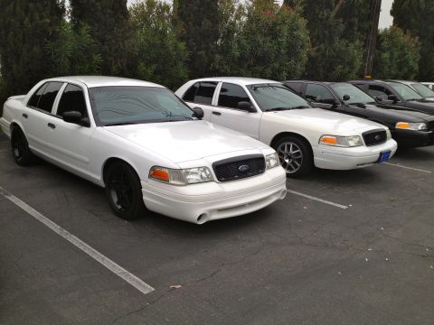 2004 Ford Crown Victoria - Several Ford Crown Victoria sedans, including two white ones in the foreground, are parked in a lot.