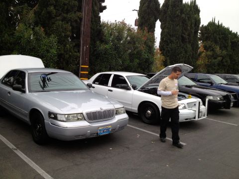 2004 Ford Crown Victoria - Several Ford Crown Victorias are parked in a lot, some with hoods open, under an overcast sky.