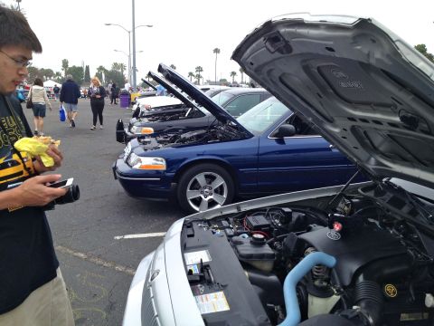 2004 Ford Crown Victoria - A line of Ford Crown Victorias are displayed with their hoods open at an outdoor car show.