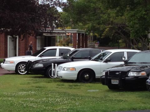 2004 Ford Crown Victoria - Several Ford Crown Victoria police cars are lined up on a grassy area in front of a building with an 'Amusement Park' sign.
