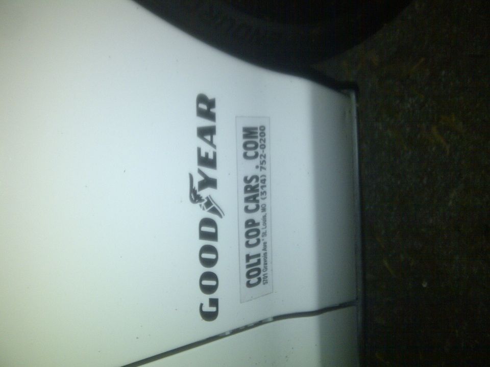 White vehicle door with Goodyear logo and Colt Cop Cars sticker. Sticker text: COLT COP CARS.COM 5701 Gravois Ave. St. Louis, MO (314) 752-0200