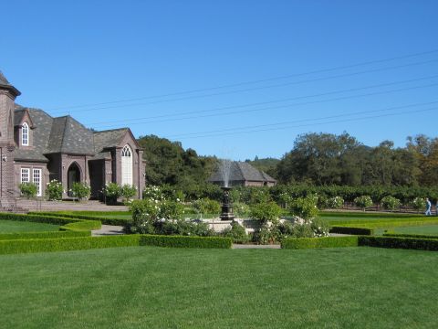 2002 Ford Taurus - A person strolls through a formal garden with a fountain and a large brick estate under a clear blue sky.