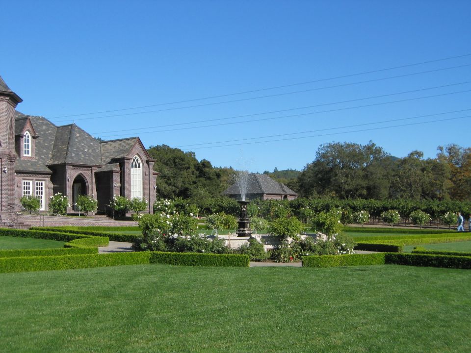 Person walking on path by fountain and brick building with manicured hedges and green lawn