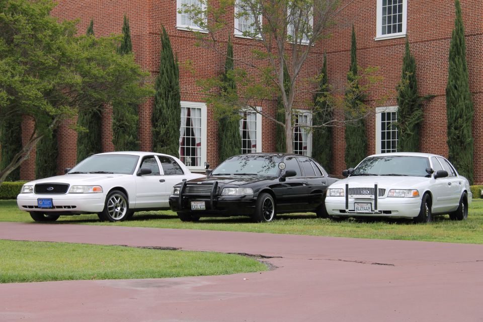 Three Ford Crown Victorias parked in front of a brick building; two white, one black