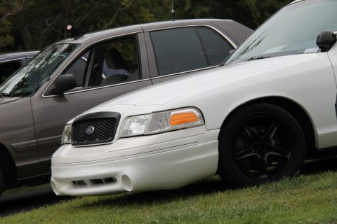 2004 Ford Crown Victoria - A white 2004 Ford Crown Victoria is parked next to a gray sedan, its distinctive front end and black aftermarket wheels.