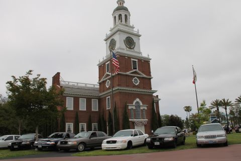 2004 Ford Crown Victoria - A collection of Ford Crown Victorias, including police and civilian models, are parked on a lawn in front of a historic building.