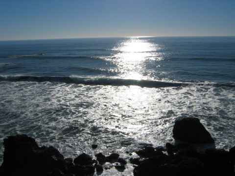 2002 Ford Taurus - Waves break on the rocky shore with the sun glinting off the ocean surface.