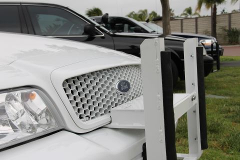 2004 Ford Crown Victoria - A white 2004 Ford Crown Victoria, equipped with a push bumper and a distinctive honeycomb grille, is parked alongside other vehicles.