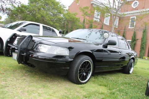 2004 Ford Crown Victoria - Black 2004 Ford Crown Victoria with push bar and aftermarket wheels is parked on grass.