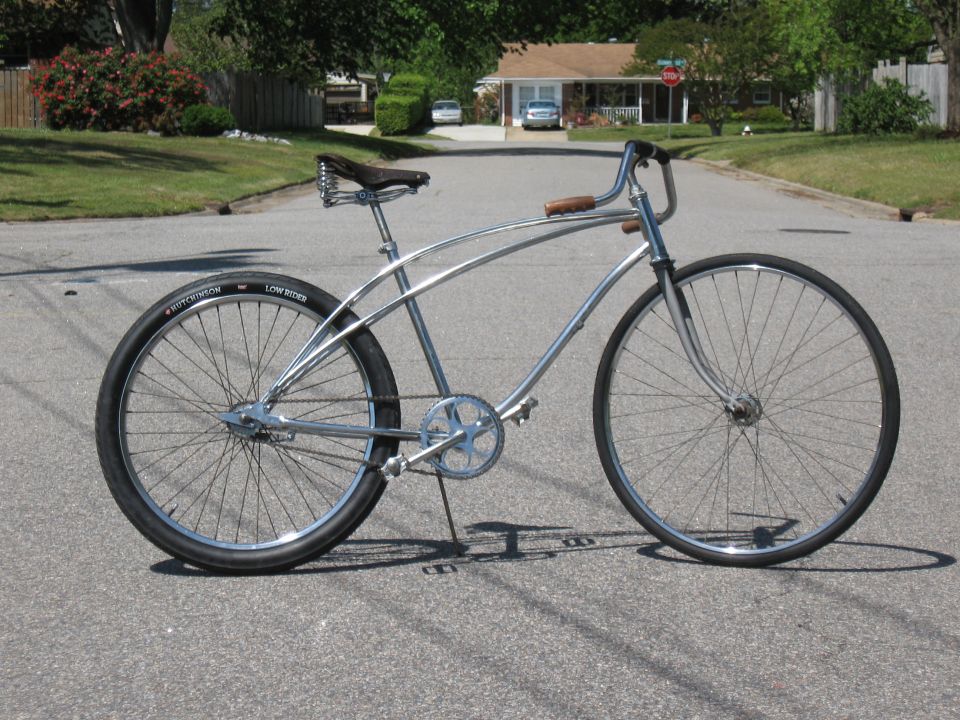 Chrome cruiser bicycle with a brown leather seat and wooden handlebars, parked on a suburban street