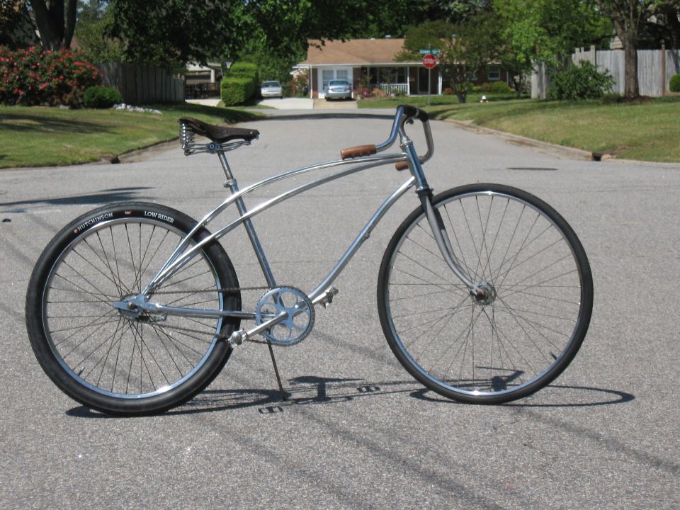 Chrome cruiser bicycle with black seat and brown handlebars, parked on asphalt