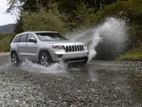 1991 Ford Crown Victoria - A silver Jeep Grand Cherokee drives through a shallow stream, creating a large spray of water.