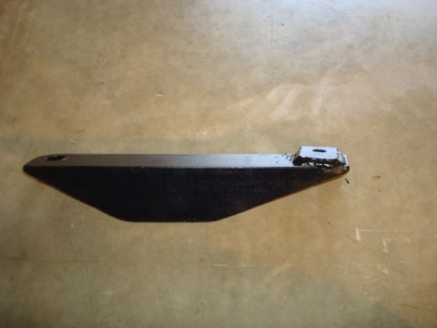 1995 Ford Bronco - A close-up view of a black metal steering linkage part resting on a concrete surface.