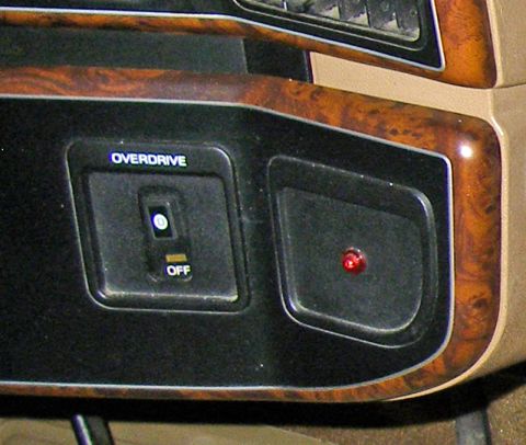 1990 Ford Bronco - The dashboard features wood grain trim around the overdrive switch and a lit red indicator light.