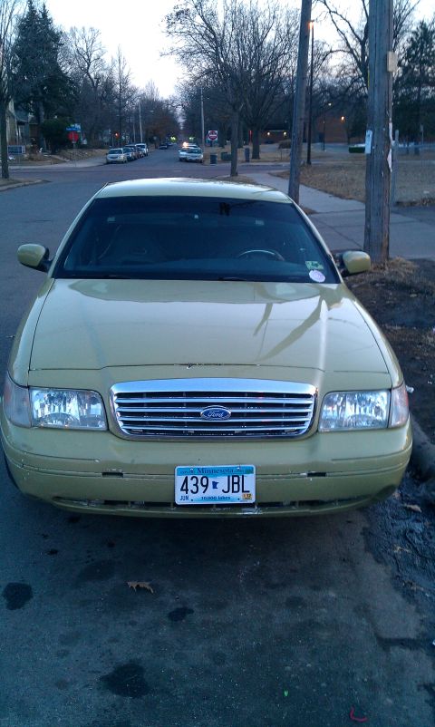2000 Ford Crown Victoria - A gold 2000 Ford Crown Victoria is parked on a residential street, facing the camera.