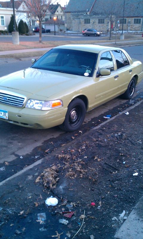 2000 Ford Crown Victoria - A tan 2000 Ford Crown Victoria is parked on the side of the road, with debris visible on the ground.