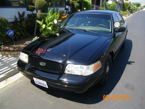 2003 Ford Crown Victoria - A black 2003 Ford Crown Victoria is parked on a street, reflecting the surrounding environment.