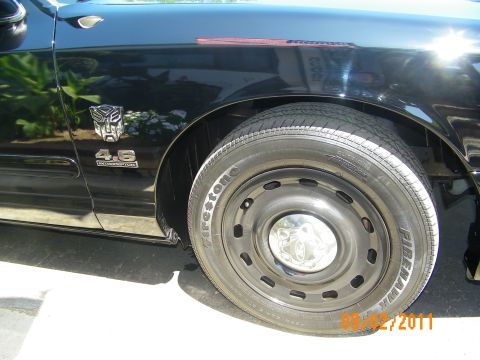 2003 Ford Crown Victoria - A close-up of a black sedan's fender and wheel shows a Transformers badge and '4.6' emblem.