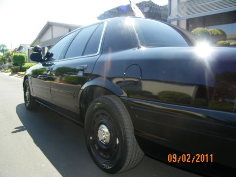 2003 Ford Crown Victoria - Low rear-side angle of a black sedan showing fuel door, tinted glass and a black steel wheel.