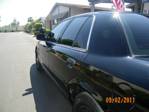 2003 Ford Crown Victoria - Right-side mid view of a black Ford sedan with chrome door handles and dark tinted glass.