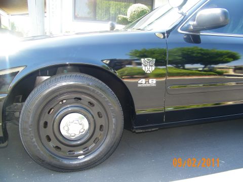 2003 Ford Crown Victoria - Front fender detail of a black sedan showing Transformers decal, 4.6 Interceptor badge and steel wheel.