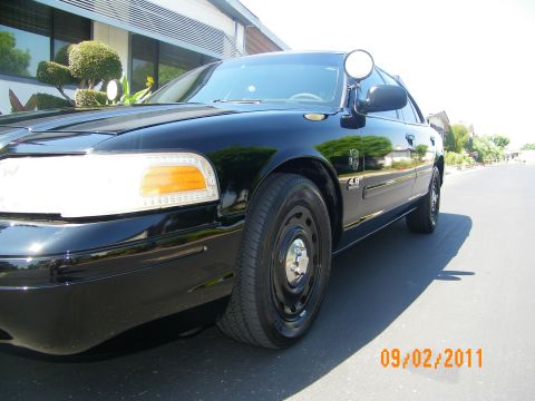 2003 Ford Crown Victoria - Low front-quarter angle of a black Ford sedan showing headlight, amber signal and black steel wheel.