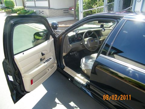 2003 Ford Crown Victoria - Driver door open on a black sedan revealing parchment cloth seats and a Ford-badged steering wheel.