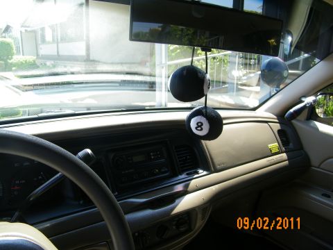 2003 Ford Crown Victoria - Front cabin view through windshield showing center stack, climate vents and dual 8-ball fuzzy dice on rearview mirror