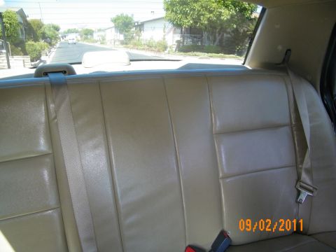2003 Ford Crown Victoria - Close view of beige rear seat upholstery and buckle with houses visible through the back glass