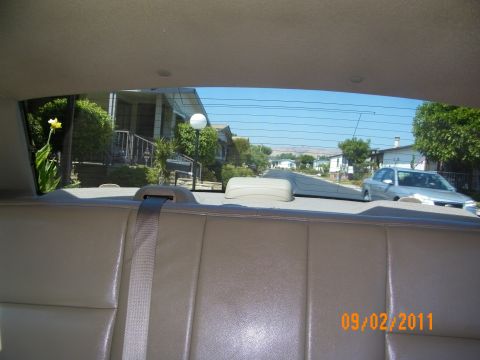 2003 Ford Crown Victoria - View over the tan rear seat toward the back glass showing a residential street and parked sedan