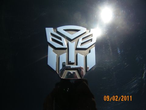 2003 Ford Crown Victoria - Polished silver Autobot face emblem catching sunlight against a dark reflective surface