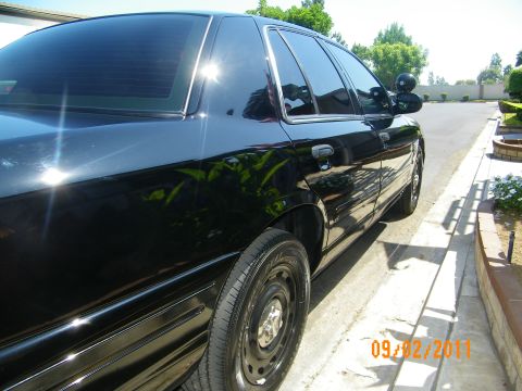 2003 Ford Crown Victoria - Side view of a glossy black four-door sedan parked along a curb with steelie wheels