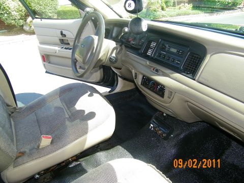 2003 Ford Crown Victoria - Driver-side view of tan dashboard, center radio, lower gauges and column-mounted shifter