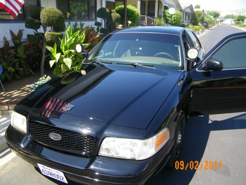 2003 Ford Crown Victoria - Front view of black sedan with Ford grille oval, pillar spotlight and flag on the hood