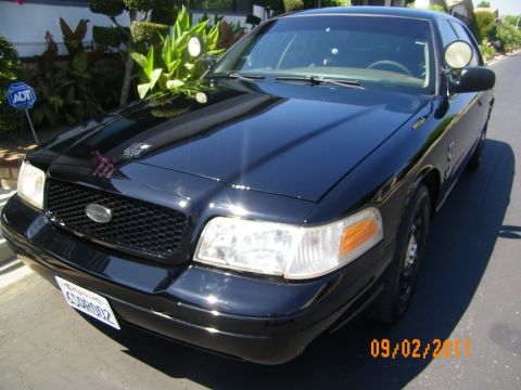 2003 Ford Crown Victoria - Front quarter of black full-size sedan showing headlights, grille oval and ADT yard sign