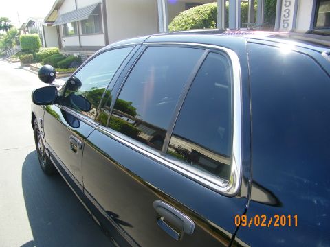 2003 Ford Crown Victoria - Close view of dark-tinted side glass, chrome window surround and door handle on a black Crown Victoria.
