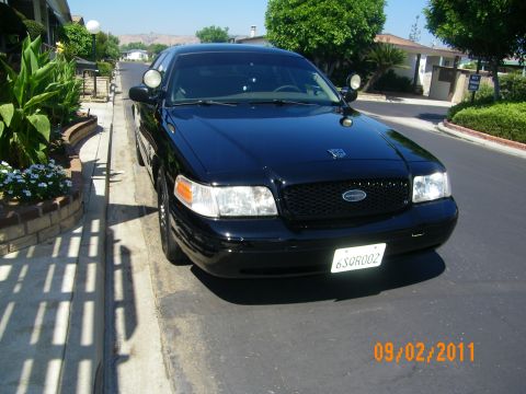 2003 Ford Crown Victoria - Front view of a black Crown Victoria P71 with spotlight, mesh grille and Interceptor emblem in a driveway.