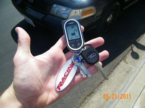 2003 Ford Crown Victoria - Palm displaying a Viper two-way LCD remote, a Ford key and a silver Ford Racing fob, sedan headlight behind.