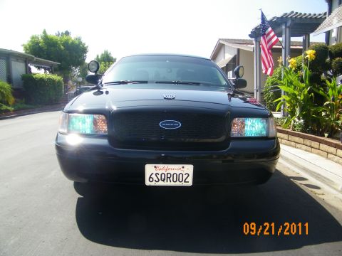 2003 Ford Crown Victoria - Head-on view of a black Crown Victoria P71 with spotlights, Interceptor grille emblem and US flag behind.