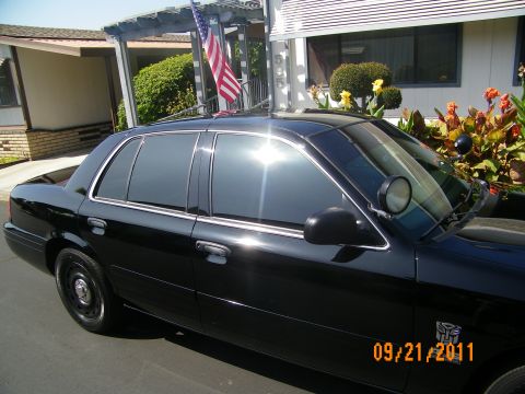 2003 Ford Crown Victoria - Side profile of a black Crown Victoria with tinted windows, pillar spotlight and Autobot decal near a home.