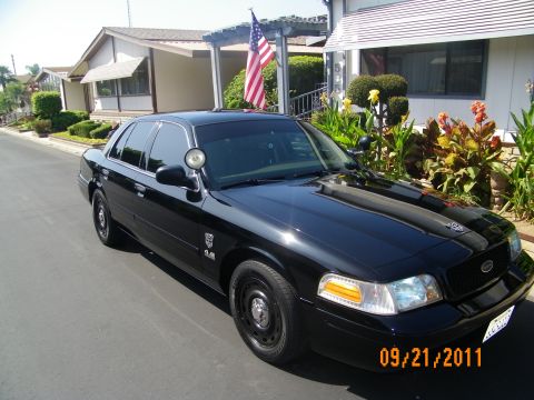 2003 Ford Crown Victoria - Front three-quarter of a black Crown Victoria parked by a home, pillar spotlight and steel wheels visible.