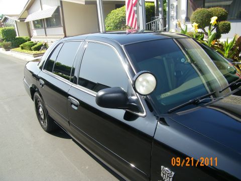 2003 Ford Crown Victoria - Detail of the passenger-side spotlight, mirror and tinted glass on a black Crown Victoria near a home.