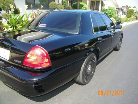 2003 Ford Crown Victoria - Rear three-quarter view of a black Crown Victoria Limited with steel wheels and red taillamp in a driveway.