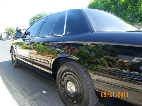 2003 Ford Crown Victoria - Low side angle of glossy black sedan with black steel wheels and fuel door, photographed on asphalt
